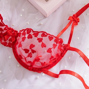 Dettaglio del reggiseno in pizzo rosso con ricamo a cuore, rete e fiocchi di nastro