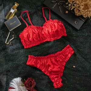 Flat lay of red satin lingerie set with ruffles, perfume and pearls on green background