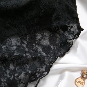 Détail de dentelle florale noire avec bords festonnés sur un fond en soie blanche douce