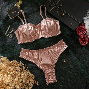 Detail of ruched satin lingerie set in lotus pink with elegant ruffled trim and smooth texture