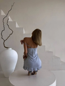 Artistic back view of a grey slip dress with ruffle hem on white minimalist steps