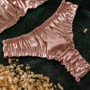 Detail of pink satin lingerie with pleated edges and silky texture against green backdrop