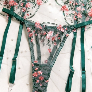 Detail of dark green floral embroidery on sheer mesh lingerie with adjustable garters