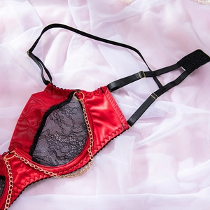 Detail of red satin bra with black lace trim and decorative gold metal chains
