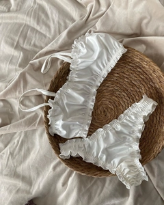 Dettaglio completo di set intimo in raso bianco con volant su vassoio in paglia intrecciata