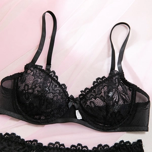 Dettaglio di lingerie in pizzo nero con ricami floreali e fiocchetto su sfondo rosa