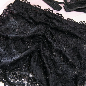 Dettaglio in pizzo floreale nero con bordi smerlati e chiusura a tre file di ganci