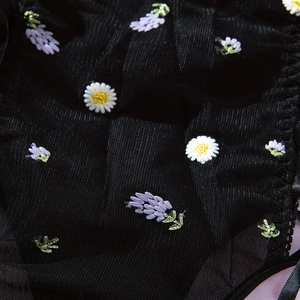 Detailed view of floral embroidery on sheer black mesh fabric with daisy and lavender motifs