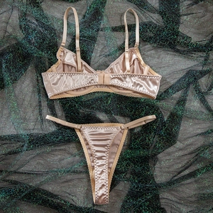 Detail of beige satin lingerie set with adjustable straps and lace trim on dark mesh