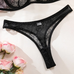 Close-up of black floral lace thong on beige background with romantic rose petal accents