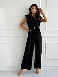Detail eines schwarzen ärmellosen Jumpsuits mit V-Ausschnitt und goldenem Metallgürtel