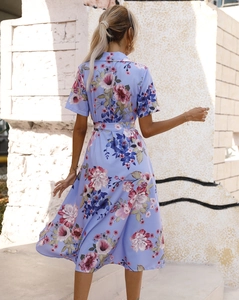 Back view of a light blue floral midi dress with waist tie in a scenic outdoor setting
