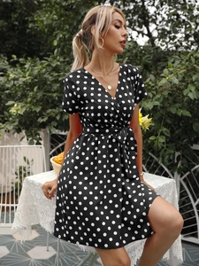 Détail d'une robe portefeuille noire à pois avec col en V et ceinture dans un jardin