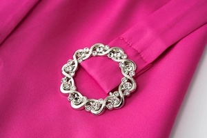 Macro shot of silver rhinestone buckle with wave pattern on rose red dress fabric