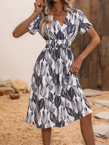 Detail of white V-neck floral dress featuring blue tropical leaf print and waist pleats