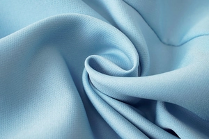 Macro du tissu textile bleu clair montrant la texture dense et le drapé de qualité