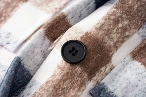 Close-up detail of vintage plaid wool coat fabric with a sewn black button and soft texture