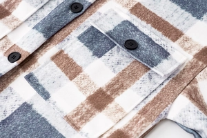 Detail of blue and brown plaid flannel jacket showing front pocket and matte black button