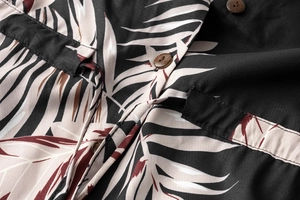 Detailed close-up of brown wooden buttons and tropical palm leaf print on black fabric