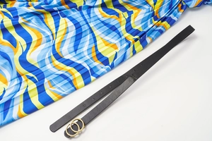 Close-up of a black leather belt with a golden double ring buckle over a pleated skirt