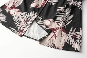 Detail of tropical leaf print on black fabric with hem stitching and button close-up