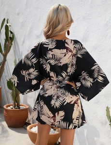 Detail of tropical leaf print dress with elastic waist and wide sleeves on black fabric
