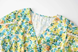 Détail de la robe à fleurs avec col en V et dentelle à pompons blancs sur l'épaule