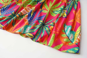 Detail of tropical leaf print summer dress fabric with vibrant pink and green floral patterns