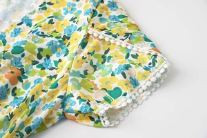 Détail de la manche d'une robe fleurie avec dentelle blanche et pompons délicats