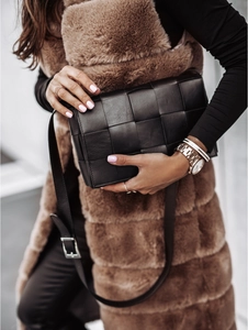 Détail d'un sac à bandoulière en cuir tressé noir porté sur un gilet en fourrure
