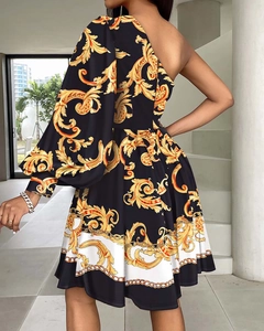 Détail du motif baroque doré et de l'épaule asymétrique sur une robe imprimée noire