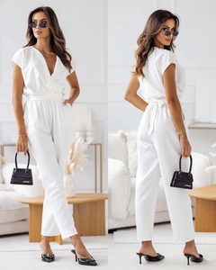 Close-up of white V-neck short sleeve jumpsuit with waist tie in a clean minimalist set