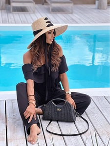 Details des schwarzen Jumpsuits mit Volants, Strohhut und Tasche vor Resort-Hintergrund