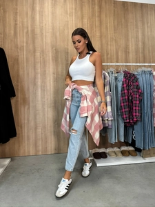 Detail of pink plaid shirt tied around waist with white tank top and ripped denim jeans