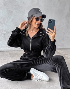 Black velvet tracksuit detail showing short zip hoodie and high-waist joggers in a sitting pose