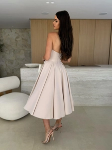 Detail of elegant champagne strapless midi dress featuring pleated satin skirt and slim fit waist