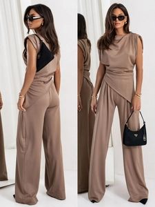 Detail view showing asymmetric draped pleats and mocha brown fabric texture of a jumpsuit