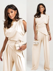 Detail of beige sleeveless jumpsuit featuring padded shoulders and asymmetric draped waist