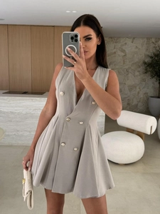 Détail d'une robe grise sans manches à col en V avec boutons dorés et jupe plissée