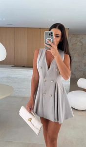 Détail d'une robe blazer grise sans manches avec boutons dorés et ourlet plissé en A