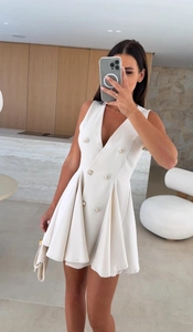 Détail de la robe blanche sans manches à col en V avec boutons dorés et jupe plissée