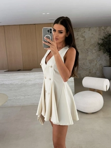 Détail d'une robe blazer blanche sans manches avec col en V, boutons dorés et jupe plissée