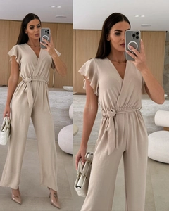 Detail of beige V-neck jumpsuit featuring ruffled sleeves and adjustable waist tie belt