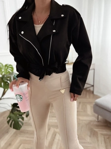 Close-up of black faux suede biker jacket with silver zippers and beige slim fit trousers
