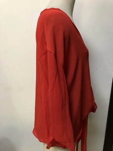 Detail of red V-neck chiffon blouse with flutter sleeves and waist tie adjustment