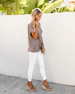 Detail of an off-shoulder brown T-shirt with side ruching worn with white ripped jeans