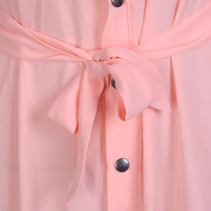 Gros plan d'une robe rose avec ceinture à nœud et détails de boutons métalliques