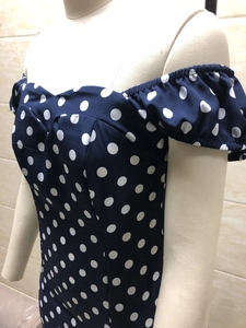 Détail de l'encolure Bardot et des manches bouffantes sur une robe moulante à pois marine