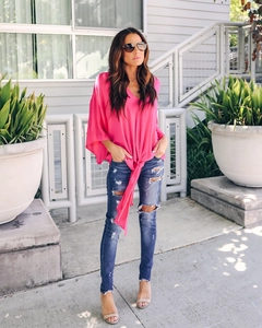 Detail of fuchsia V-neck chiffon top with a stylish knot hem and distressed skinny blue jeans