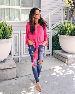 Detail of rose red V-neck chiffon blouse with tie-waist and flutter sleeves on denim